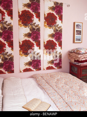 Kleine rosa Schlafzimmer mit roten Rose gemustert Stoffbahnen an Wand über dem Bett mit weißem Leinen und Vintage Pastell Blumen Eiderdaune Stockfoto