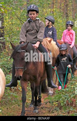 Kinder auf ihren Ponys durch einen Wald reiten Stockfoto