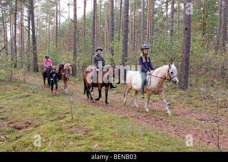 Kinder auf ihren Ponys durch einen Wald reiten Stockfoto