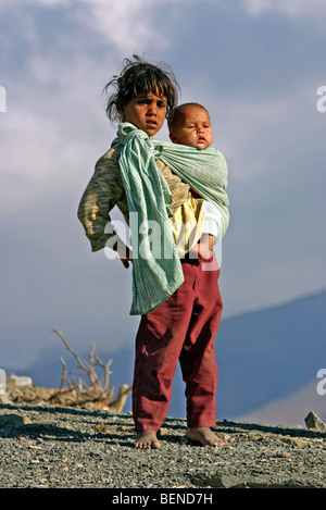 Semi-Berber Nomadenkinder, Mädchen tragen kleine Baby Bruder in Schlinge in das Atlasgebirge, Marokko, Nordafrika Stockfoto