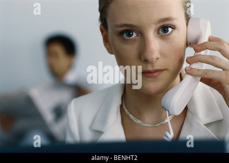 Junge Geschäftsfrau hält Telefon zum Ohr, Blick in die Kamera Stockfoto
