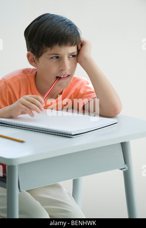 Grundschüler sitzen am Schreibtisch, stützte sich auf Ellbogen, Ende der Bleistift kauen Stockfoto