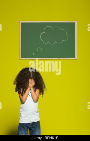 Kleines Mädchen für Gesicht mit den Händen, dachte Blase an Tafel hinter ihr Stockfoto