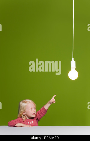 Kleines Mädchen zeigte auf leuchtende Glühbirne ausgesetzt overhead Stockfoto