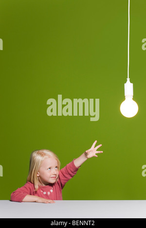 Kleines Mädchen für leuchtende Glühbirne erreichen ausgesetzt overhead Stockfoto