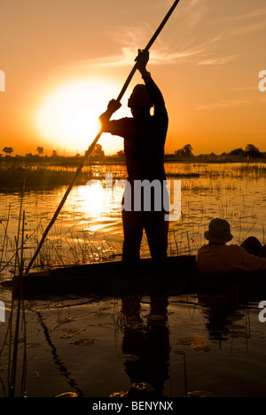 Ein Boot bewegt sich entlang des Okavango-Deltas bei Sonnenuntergang, Botswana, Afrika. Stockfoto