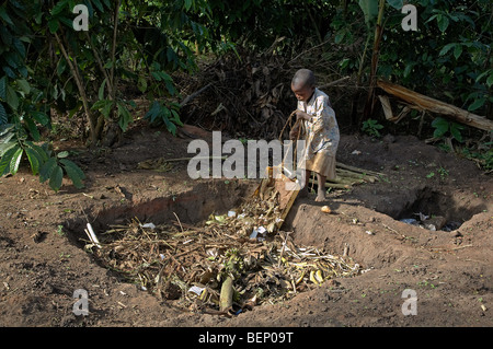 UGANDA im Hause des Najjemba Teopista, Kasaayi Dorf, Kayunga Bezirk. Kevin, 5, dumping Müll in das Loch der Abfallentsorgung Stockfoto