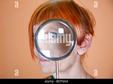 Rote behaarte Frau mit blauen Augen spähte durch ein Vergrößerungsglas Stockfoto