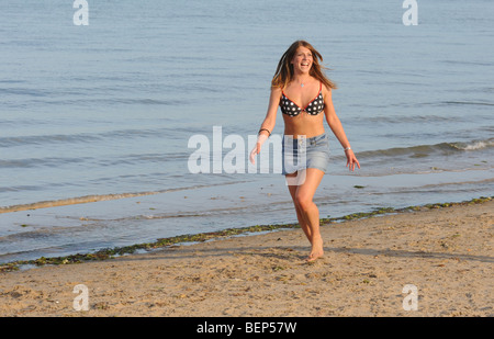 Schöne junge Frau mit langen fließenden Haaren, die entlang der weißen Sandstrand in Dorset, England Stockfoto