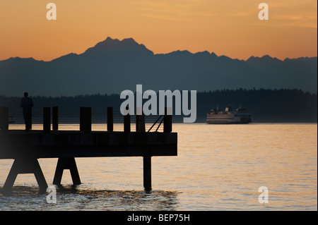 Auf Alki Beach in West Seattle, Washington geht die Sonne über die Olympic Mountains und Bainbridge Island. Fähre zur Insel. Stockfoto