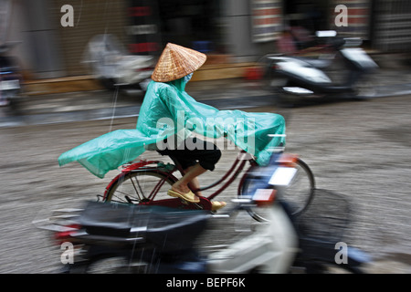 Schwenken die Straßenszene. Frau mit traditionellen konischen Hut mit ihrem Fahrrad unter dem Regen in Hanoi Hauptstadt von Vietnam, Asien Stockfoto