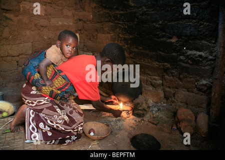 BURUNDI Frau Wied Feuer zum Kochen in ihrer Küche, während sie ein Kind auf dem Rücken trägt. Gitera. Stockfoto