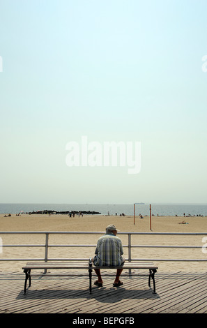Ein Mann sitzt auf einer Bank an der Coney Island-Promenade und Blick auf den Atlantischen Ozean. Stockfoto