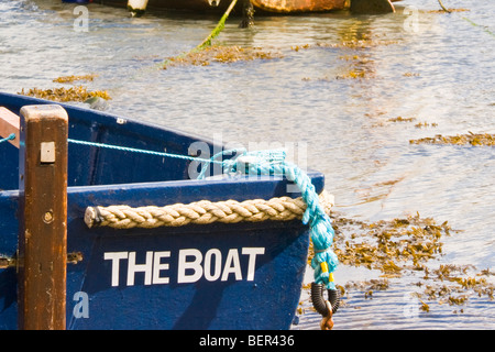 Nahaufnahme eines blauen Bootes mit dem Namen „DAS BOOT“ auf der Seite, mit einem Seil in flachem Küstenwasser gebunden. Stockfoto