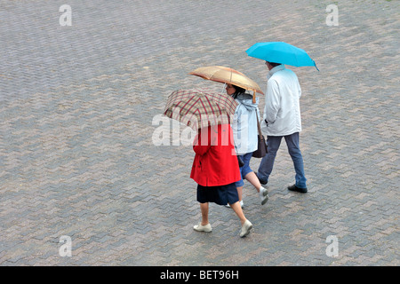 Touristen mit Regenschirme und Regenmäntel an regnerischen Tag im Regen im Badeort an der Küste entlang zu Fuß während der Sommerferien Stockfoto