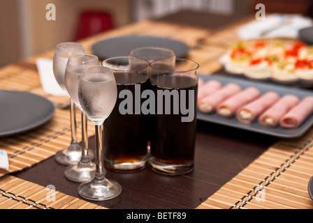 drei Gläser mit kalten Wodka und drei Gläser Cola und Snacks auf den Tisch Stockfoto