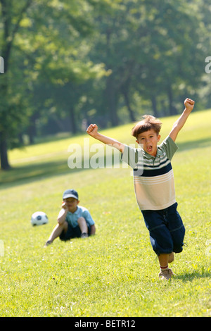 zwei Jungs spielen Fußball im Park, feiert man mit seinen Händen in der Luft Stockfoto