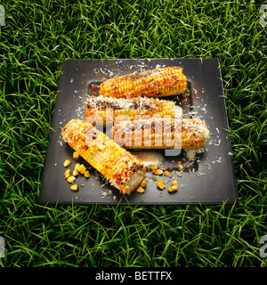 Gegrillte Maiskolben mit Käse, Butter und Chili auf einem Rasen-Hintergrund. Stockfoto