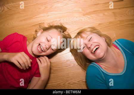 Zwei Schwestern Lachen hysterisch auf einen hölzernen Fußboden, 11 und 14 Jahren Stockfoto