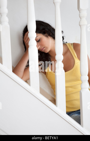Attraktive junge dunkelhaarige Frau mit Hand am Kopf gedrückt, sitzt auf der Treppe Stockfoto