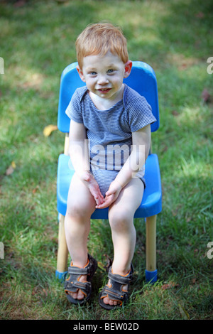 Junge sitzt auf einem Stuhl außerhalb Stockfoto
