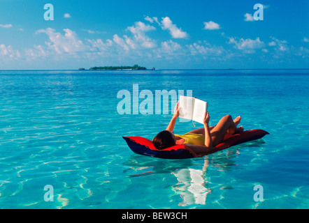 Frau auf Luftmatratze im klaren ruhigen Aqua Wasser des Indischen Ozeans mit Malediven Insel im Abstand Stockfoto