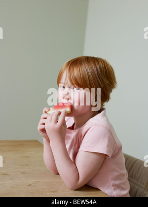 7-8 jährige lächelt Mädchen, als sie ein Stück Melone isst Stockfoto