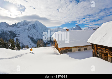 Frau mit Ski auf einer verschneiten Alm mit Holz Häuser, Zederhaus, Salzburg, Österreich Stockfoto