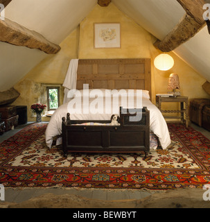 Antikes Holz Wiege unter Bett mit geschnitzten hölzernen Kopfteil in Schlafzimmer mit großen gemusterten Teppich und Holzbalken Apex Decke Stockfoto