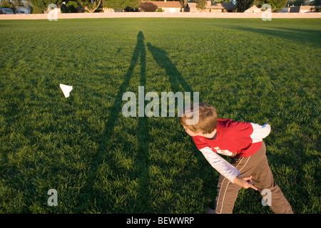 ein Junge wirft einen Papierflieger in der Luft in einem Park, Sonnenuntergang Stockfoto