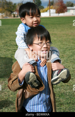 zehn Jahre alten japanischen Jungen trägt seinem drei Jahre alten Bruder auf seinen Schultern, im Freien in einem park Stockfoto