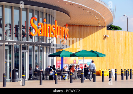 Vor der façade des Sainsburys Supermarkt sitzen Menschen im Starbucks Café unter Sonnenschirmen Greenwich London England UK Stockfoto