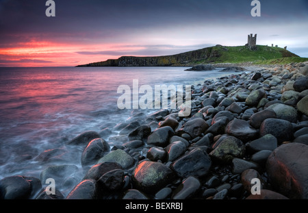 Das rosa vor der Morgendämmerung leuchtet das Meer und die Graymare Felsen am Dunstanburgh Castle. Stockfoto