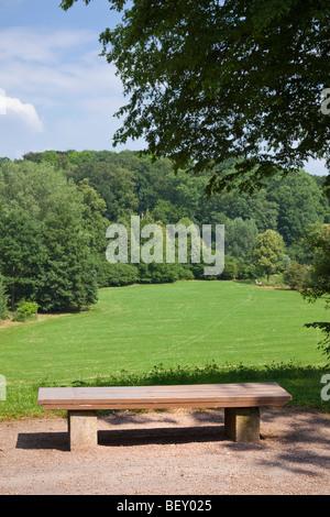 Hölzerne Parkbank mit Blick auf ein Feld und Wald in einem urbanen City-park Stockfoto