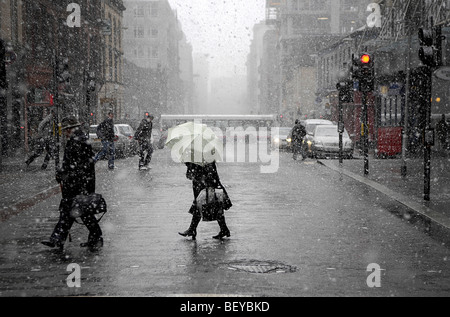 Eine Frau mit einem Regenschirm kreuzt West Nile Street, Glasgow während eines Schneesturms. Stockfoto