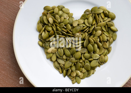 Kürbiskerne in Form eines Herzens auf einem weißen Teller und Tisch aus Holz Hintergrund Stockfoto
