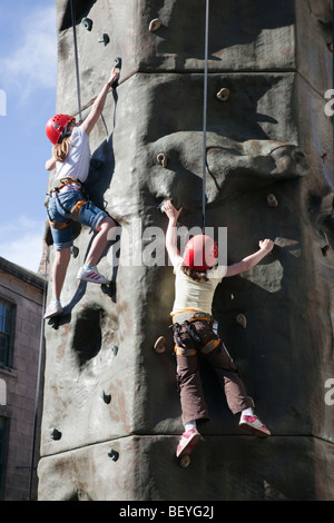 Kinder lernen, Felsen klettern auf künstliche Kletterwand im Freien in einem Fundraising-Event. England-UK Stockfoto