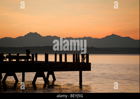 Fotograf auf einen Alki Beach Pier in West Seattle, Washington. Die Sonne geht über die Olympic Mountains und Bainbridge Island. Stockfoto