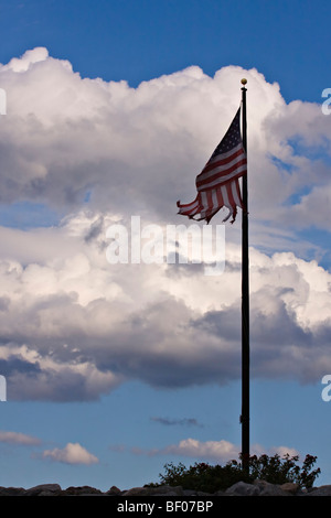 Amerikanische Flagge, die zerschlagen und zerrissen auf eine Fahnenstange mit blauen Himmel und Wolken im Hintergrund. Stockfoto