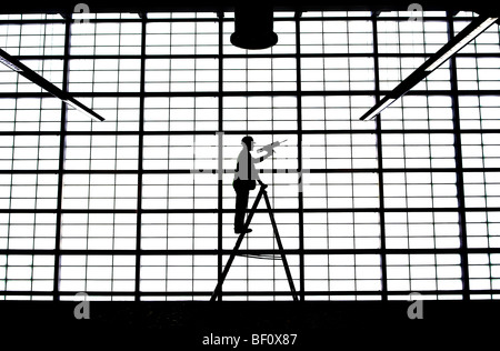 Ein Mann auf einer Leiter verleiht den letzten Schliff eine große undurchsichtige Wand in der Abflughalle im Flughafen von Glasgow, Schottland. Stockfoto
