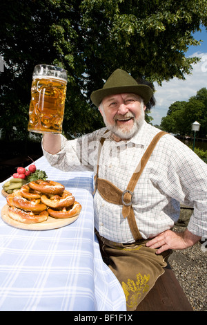 Ein traditionell gekleidet deutscher Mann in einem Biergarten Anhebung Bierglas in toast Stockfoto