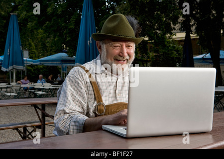 Ein traditionell gekleidet deutscher Mann in einem Biergarten mit einem laptop Stockfoto