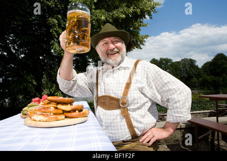 Ein traditionell gekleidet deutscher Mann in einem Biergarten Anhebung Bierglas in toast Stockfoto