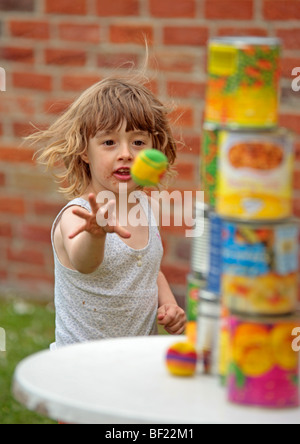 ein junges Mädchen, einen Ball zu werfen, um eine Pyramide aus Dosen bei einem Kindergeburtstag Stockfoto