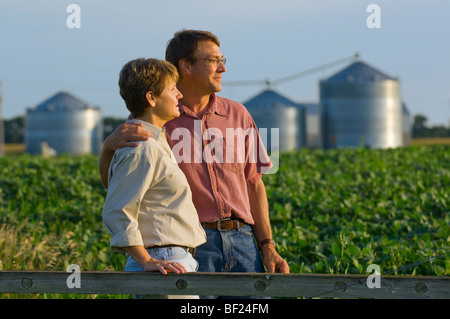 Mann und Frau Bauern in ihrem Soja-Bereich einige persönliche Momente miteinander teilen, mit Getreidesilos im Hintergrund / USA. Stockfoto