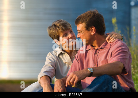 Mann und Frau Landwirte zusammen sitzen einige persönliche Momente gemeinsam mit Getreidesilos im Hintergrund / USA. Stockfoto