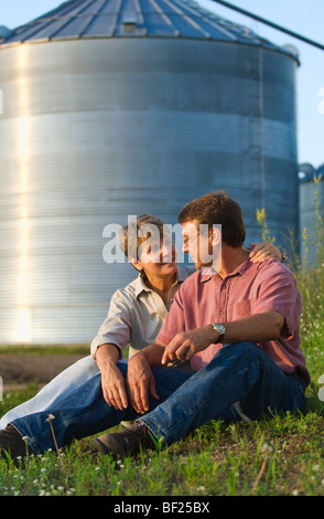 Mann und Frau Landwirte zusammen sitzen einige persönliche Momente gemeinsam mit Getreidesilos im Hintergrund / USA. Stockfoto