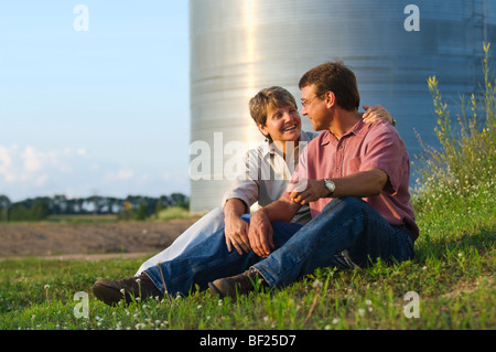 Mann und Frau Landwirte zusammen sitzen einige persönliche Momente gemeinsam mit Getreidesilos im Hintergrund / USA. Stockfoto