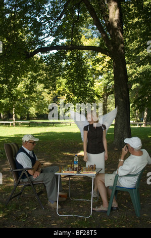 Engel, junge Frau mit Flügeln beobachten zwei Männer spielen Schach im Park, München, Bayern, Deutschland Stockfoto