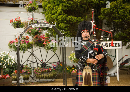 Kaukasischer schottischer Pfeifer, der vor dem Geschäft von Gretna Green Old Blacksmith, Schottland, Dudelsäcke spielt. VEREINIGTES KÖNIGREICH Stockfoto